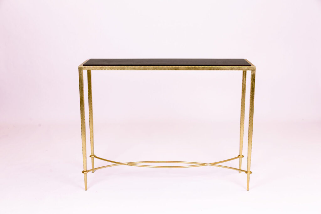 Gold metal-framed console table with a dark rectangular top, set against a pale backdrop.