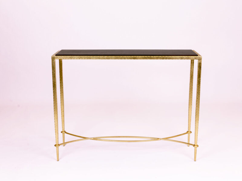 Gold metal-framed console table with a dark rectangular top, set against a pale backdrop.