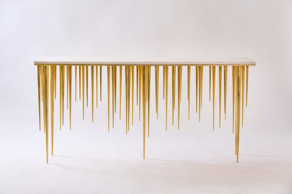 Golden console table with many slender, pointed legs resembling spikes against a plain white backdrop, minimalist gallery style.