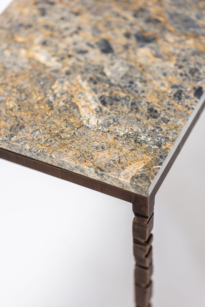 Close-up of a marble tabletop with gray, white, and gold veining and a dark brown metal leg.