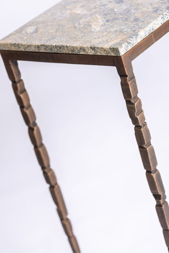 Close-up of a stone-topped table with dark brown, segmented metal legs viewed from the side.