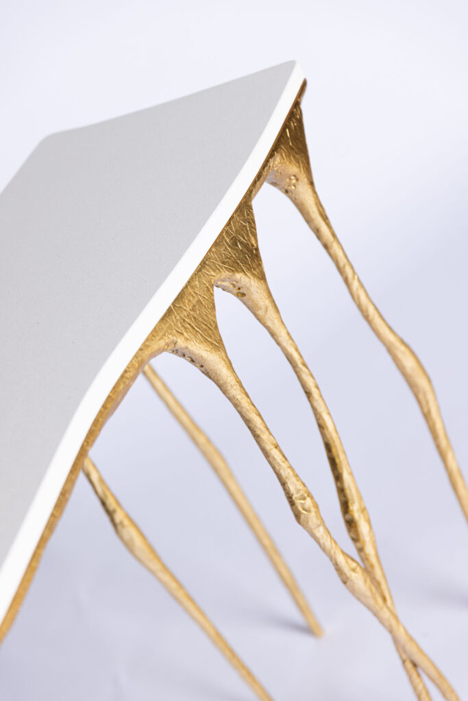 Close-up of a white, triangular edge resting on gold, sculpted legs of a modern chair.