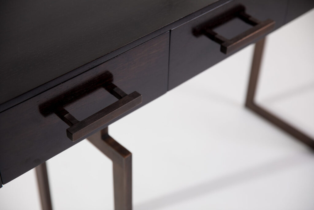 Close-up of a dark wooden desk drawer with square bronze handle components visible on a sleek surface.