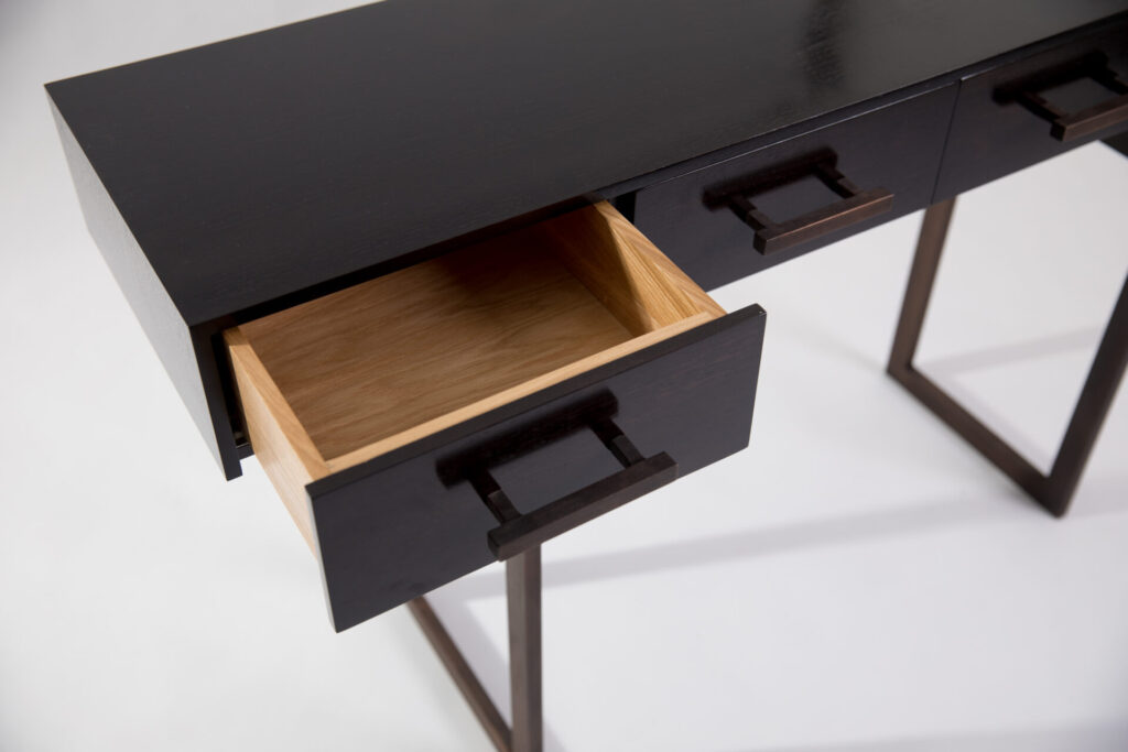 Black wooden desk with three drawers; the middle or bottom drawer is pulled out to show light natural wood interior.