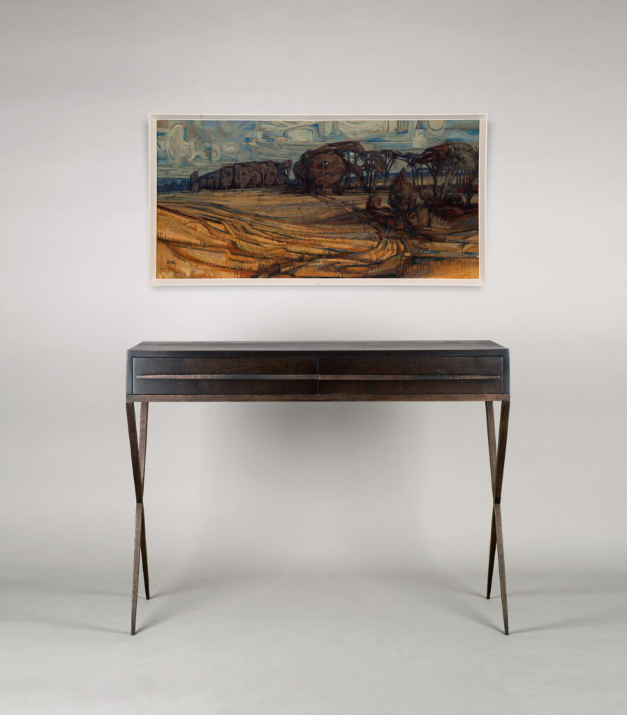 Framed landscape painting hanging on a light wall above a dark wooden console table with angled legs.