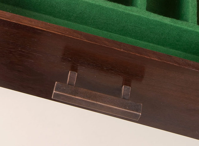 Close-up of a dark wooden box with a metal drawer pull and green felt lining visible inside.